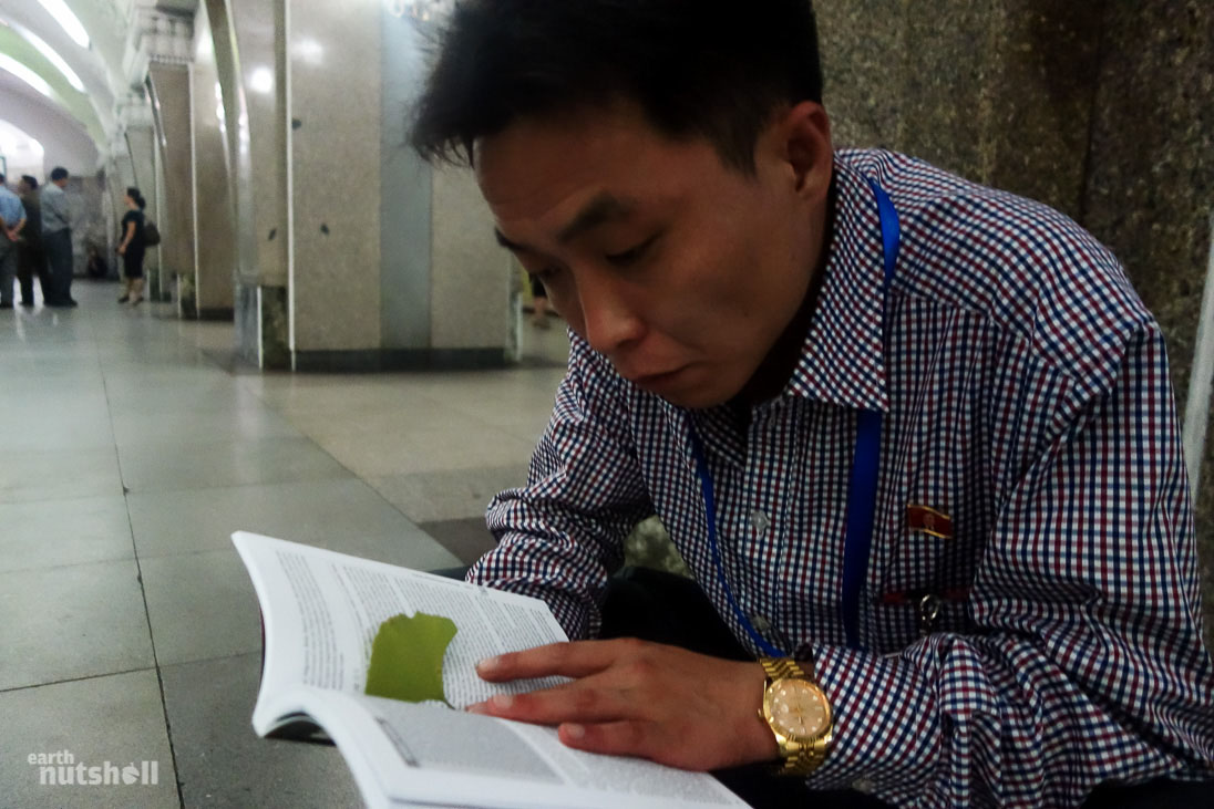 One of our guides reading an (allowed, cleared by customs) guidebook on North Korea that one of us brought across the border. He was fascinated to read an outside perspective on his beloved country. Photo taken in the Pyongyang Metro.