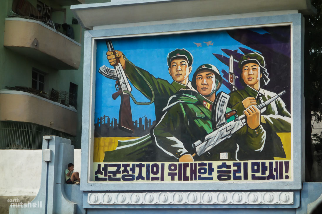 A young boy sits innocently within a giant militaristic propaganda mural in the city of Haeju. It says “Long live the great victory of Songun (military-first) politics!”